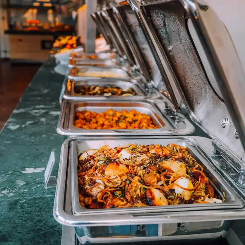 Línea de buffet con bandejas calientes abiertas y platos servidos para un evento