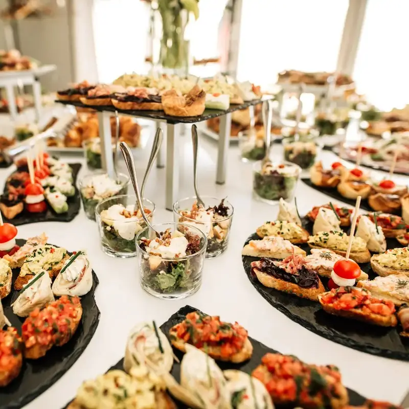 Estación de pasabocas con bruschettas, rollitos, vasitos de ensalada y brochetas sobre bandejas de pizarra