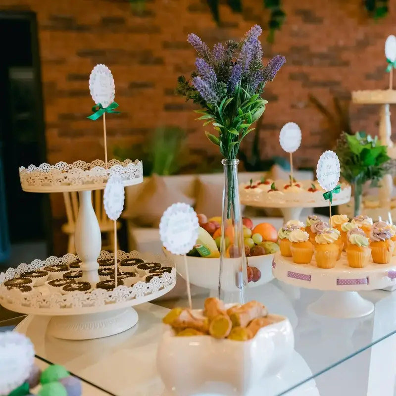 Mesa de postres con cupcakes, mini tortas, fruta y cannoli en bases blancas